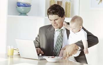 A picture of a dad who is trying to work, eat breakfast, and hold a baby.