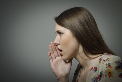 A picture of a women speaking in a hush tone with her hand cupping her mouth.