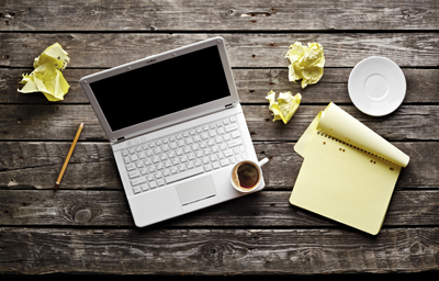 A picture of a computer sitting on a picnic table with a cup of coffee and a pad and pencil.